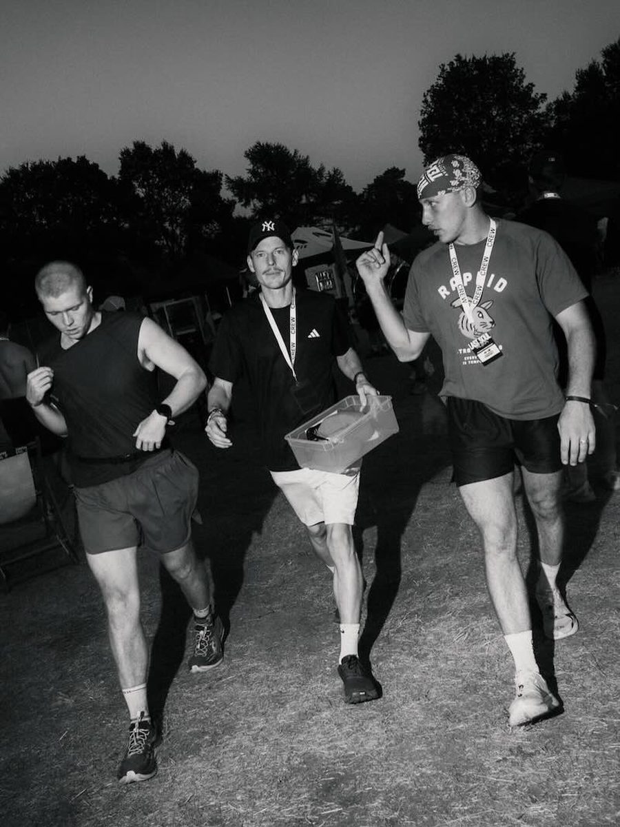 Two crew members walking a runner back through camp at dusk during a backyard ultra
